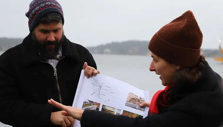 Två personer visar skisser över ett byggprojekt på Vaxholms kaj.