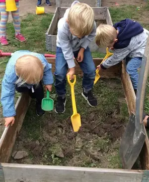 Tre förskolebarn gräver i en pallkrage.