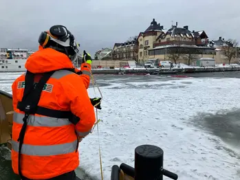 Ryggen på en man i arbetskläder med isbelagd fjärd och Vaxholms hotell i bakgrunden.